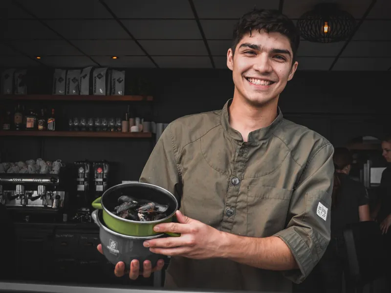 A restaurant owner holding a pot in his dining room.