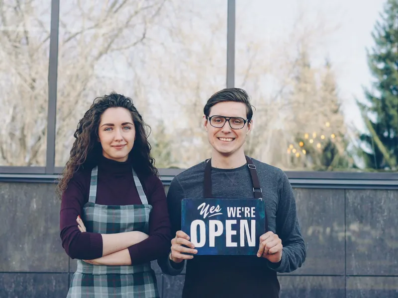 Two shop owners holding a sign that says they&rsquo;re open.
